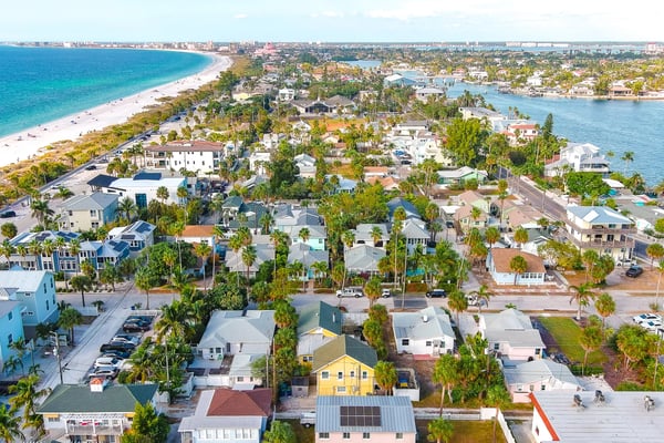 Aerial view of beachfront neighborhood with colorful homes, palm trees, sandy beach, and turquoise water