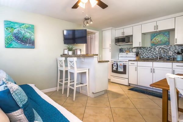 Open-plan kitchen and living area with white cabinets, tile backsplash, bar seating, and sea turtle artwork on walls